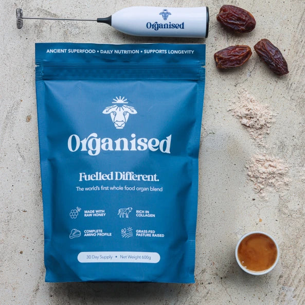 Pink smoothie in a swirl-patterned glass with toppings, surrounded by bowls and a blue package.