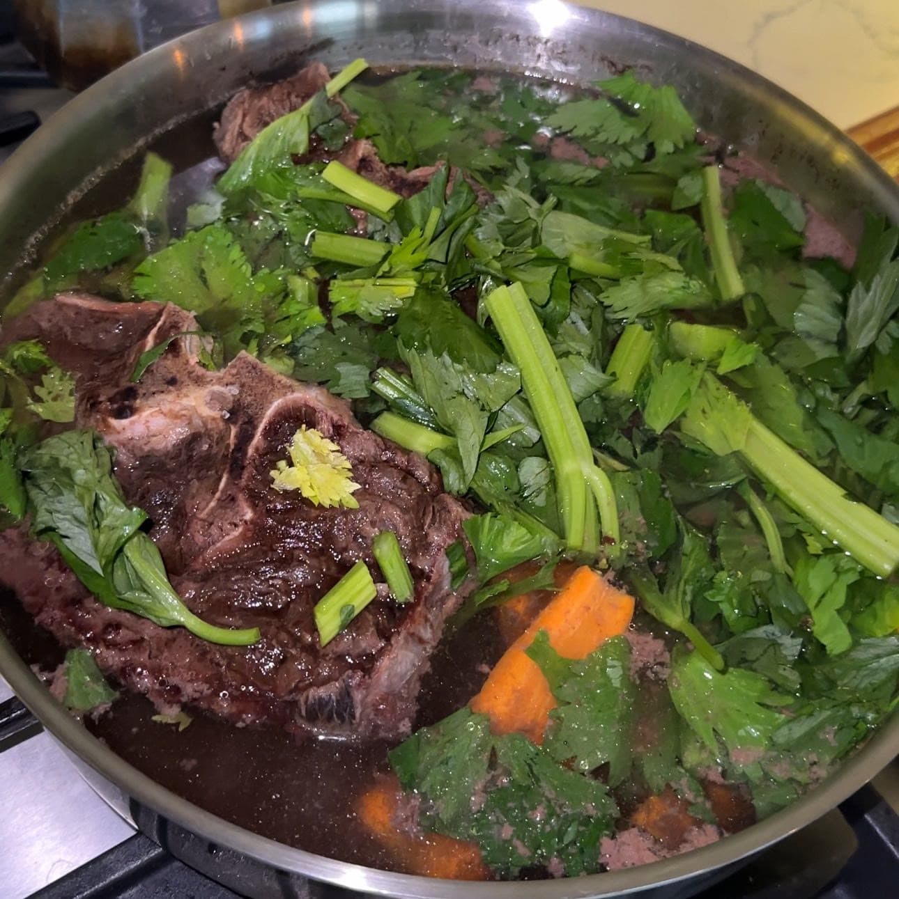 Oxtail simmering in a pan of stock with celery leaves and carrots