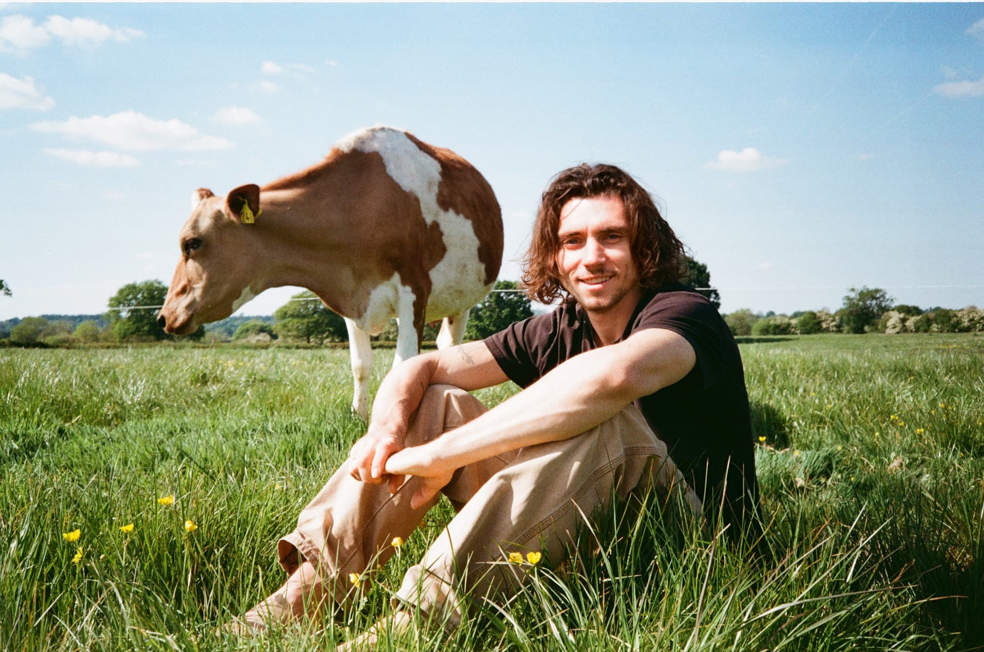 Our founder sitting in the long grass beside a curious cow